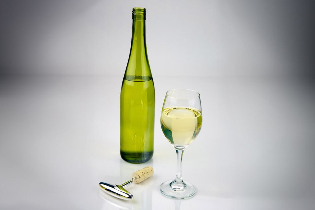 Botella de vino blanco y a su lado una copa de vino blanco